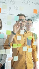 Business people team brainstorming, sharing strategy on glass whiteboard with colorful sticky notes, working collaboratively in bright office