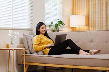 Obraz premium Photo of pretty young asian woman sit couch video call or work on laptop wear yellow pullover loft interior apartment indoors 