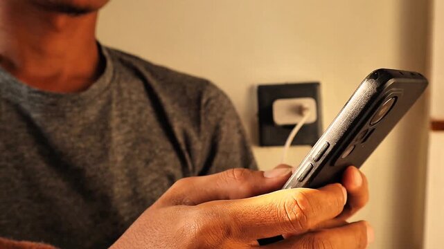 Close up of a man's hand playing a mobile game while charging his cell phone