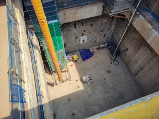 Obraz premium Deep construction excavation pit with safety barriers, ventilation ducting, and equipment, showing underground structural work and project development progress.