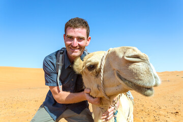 Adult man posing close to a camel in the desert, Oman