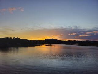 Obraz premium Serene sunset over calm water with distant hills and clouds