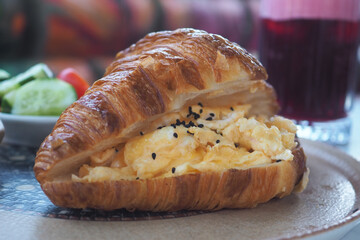 Delicious croissant sandwich with scrambled eggs and salad