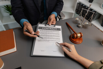 A male lawyer in a suit discusses contract details with a female client, pointing to the signature...