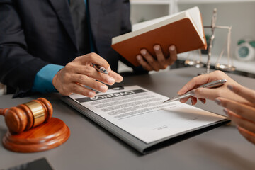 A male lawyer in a suit discusses contract details with a female client, pointing to the signature...