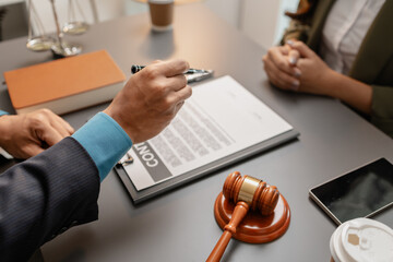 A male lawyer in a suit discusses contract details with a female client, pointing to the signature...