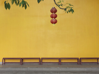 Red Lanterns Hanging in Front of a Yellow Wall with Benches Below