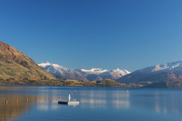 May 18, 2025: Stunning Lake Wanaka, South Island, New Zealand, with the majestic snow-capped Southern Alps reflecting in the clear blue water with swimming pier in the center. Tranquil alpine scenery.