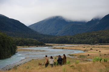 Group of peoples stand on rocks overlooking the winding turquoise Makarora River, framed by lush mountains under a cloudy sky, on New Zealand's South Island, in May 2025.