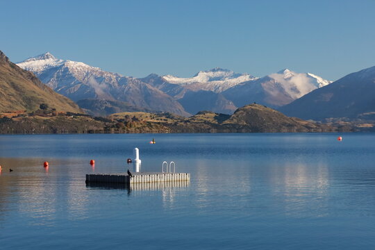 May 18, 2025: Stunning Lake Wanaka, South Island, New Zealand, with the majestic snow-capped Southern Alps reflecting in the clear blue water with swimming pier in the center. Tranquil alpine scenery.