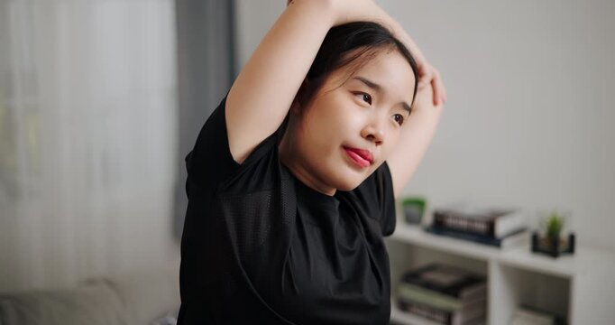 Handheld selective focus shot, Relaxed Asian woman is exercising by stretching in the living room at home. Healthy Lifestyle Concepts. Women Lifestyle