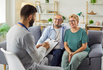 Home health consultation: a smiling doctor reviews notes with a senior couple on sofa, discussing...