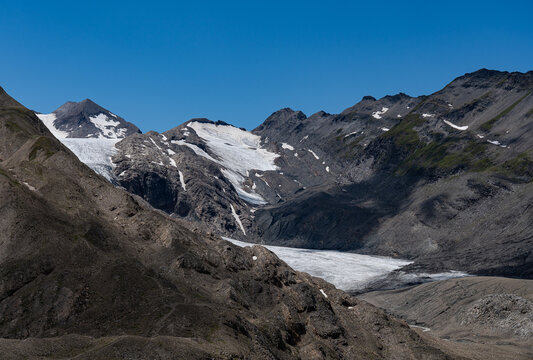 Turquoise Gries Lake and glacier near Corno-Gries Pass in the Swiss Alps. Stunning alpine landscape with rugged peaks, hiking trails, and wildflowers under a bright summer sky.