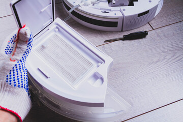Maintenance of the robot vacuum cleaner. Replacement of brushes and filter. The master repairs the vacuum cleaner. Gloves and a master's tool.