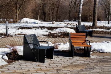 Wooden bench in the spring park. Bright spring sun and snow in the park. Place to rest for a walk. Morning walk..