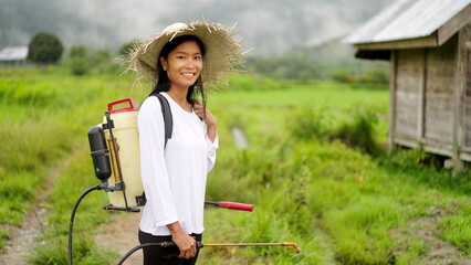 portrait, smiling asian woman rice farmer with pesticide spraying on field or plantation, looking...