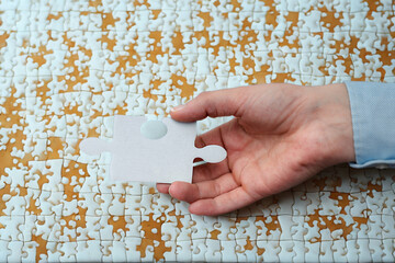 Hand holding a single white puzzle piece against a completed puzzle background