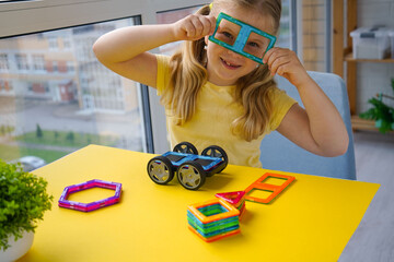 A young girl is assembling magnetic building blocks against a yellow backdrop.