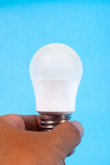 A hand holding a modern white LED light bulb against a light blue background. Concept for ideas, innovation, lighting technology, or energy efficiency.