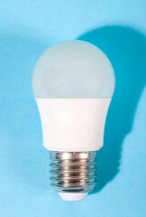 A modern, white LED light bulb isolated against a plain light blue background. A concept for ideas, innovation, illumination, energy saving, and technology.