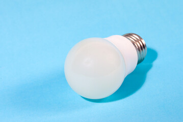 A modern, white LED light bulb isolated against a plain light blue background. A concept for ideas, innovation, illumination, energy saving, and technology.