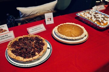 Holiday dinner buffet with pecan pie pumpkin pie sweet potatoes and green beans on red tablecloth. Thanksgiving or Christmas in cozy indoor evening setting warm festive atmosphere
