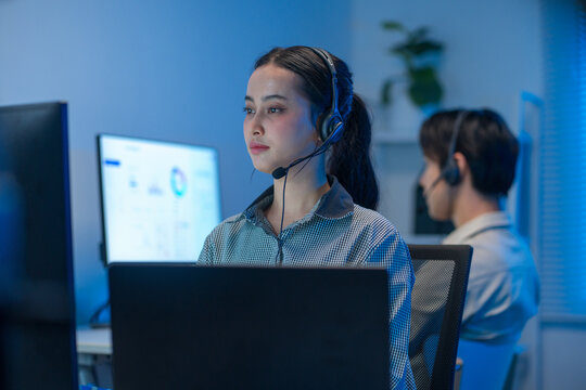 Asian IT support analyst focused on solving technical issues while wearing professional headset at office desk.
