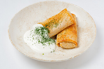 Two blini rolls are adorned with dill and paired with creamy sour cream