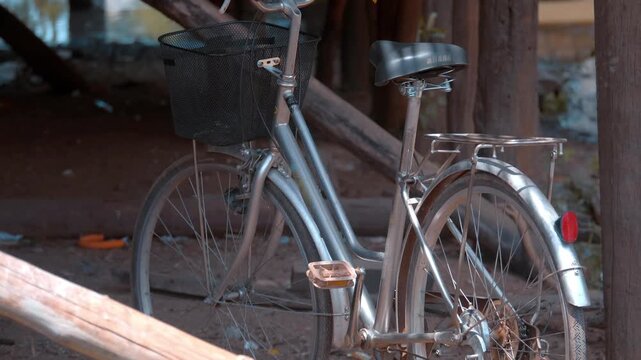 A metallic color bicycle with a basket is parked near the wooden stilts of a fisherman's house in the famous Kampong Phluk floating village, Cambodia