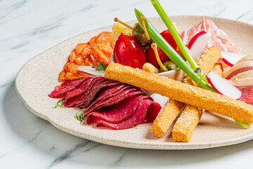 Cured meat, pickled items, and breadsticks sit on a tan plate, ready to be eaten