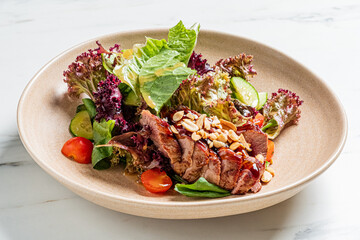 Grilled pork loin salad with tomatoes, cucumbers, lettuce, and peanuts sits on a beige plate