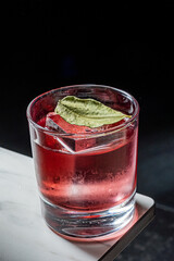 A cool, red cocktail sits on ice. A green leaf garnishes the drink, promising a burst of flavor