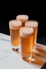 Tall glasses of beer stand on a white surface with a dark background