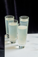 Four shot glasses are filled with pale lemonade. They stand on a marble surface