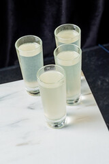 Four shot glasses, filled with a clear liquid, sit poised on a white surface
