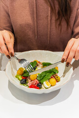 Hands hold utensils, cutting a Nicoise salad