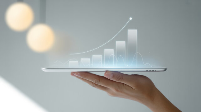 Minimalist business growth concept on light gray background, hand holding tablet with glowing holographic bar and line charts showing upward trend, modern data visualization. - Powered by Adobe