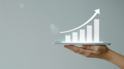 Minimalist business growth concept on light gray background, hand holding tablet with glowing holographic bar and line charts showing upward trend, modern data visualization.