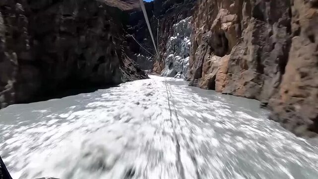 POV looking down as a person zip-lines across a chasm filled with flowing liquid mercury. High-adrenaline, quick camera movements