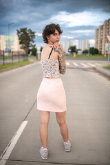 Obraz premium Young woman with short hair and floral crop top poses confidently on urban street, showcasing modern fashion style and vibrant city atmosphere with blurred background