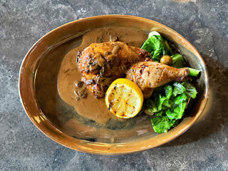 Close up grilled chicken with marinated seasoning and herbs, with mushroom sauce, rosemary, and thyme. Served with lettuce and baby potatoes. Isolated on a grey marble table.