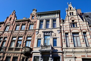 Row of ornate, eclectic European townhouses featuring varied facades, including red brick and white stone, with intricate gables in Antwerp, Belgium