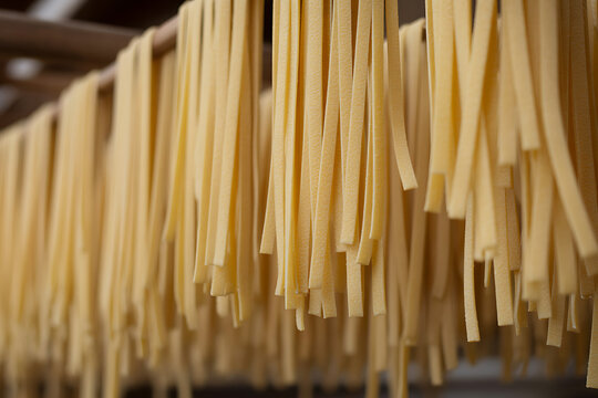 Freshly made fettuccine pasta hanging to dry on wooden rods in a rustic setting - Powered by Adobe