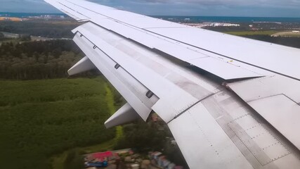 An airplane wing with movement ailerons and flaps as it lands on an airport runway