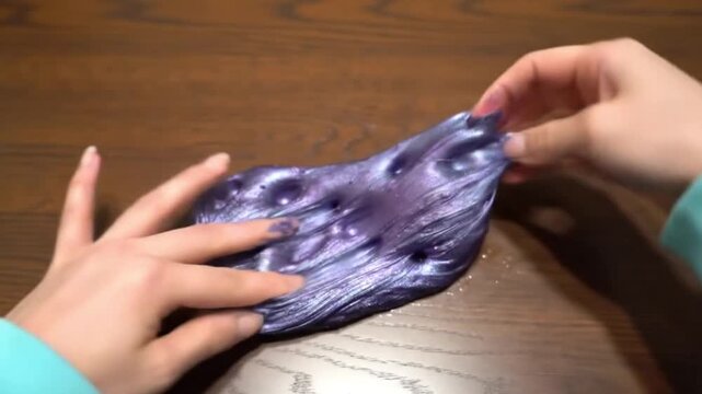 Hands stretching and playing with a blue glitter slime on a wooden surface indoors