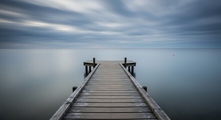 Fototapeta premium Long Wooden Pier Extending into a Misty, Calm Ocean Under a Cloudy Sky.