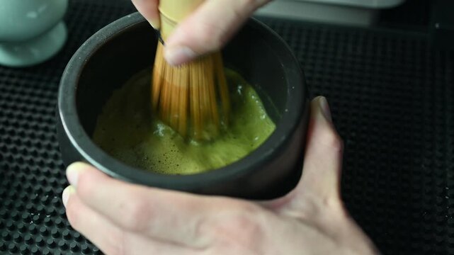 Someone using a bamboo whisk for whisking Matcha powder for drink. Whisking matcha is essential to break up clumps, create a smooth, creamy texture, and form a frothy foam on top by incorporating air.