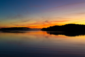 Golden sunrise over calm autumn sea with forest on the shore and gentle fog above the water, peaceful natural seascape and morning atmosphere