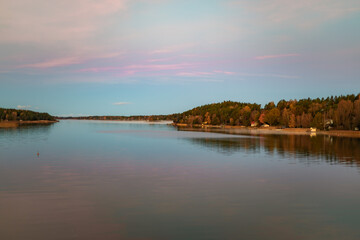 Golden sunrise over calm autumn sea with forest on the shore and gentle fog above the water, peaceful natural seascape and morning atmosphere