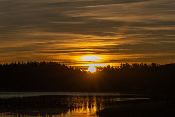 Golden sunrise over calm autumn sea with forest on the shore and gentle fog above the water, peaceful natural seascape and morning atmosphere